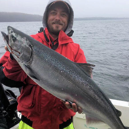 angler dressed for cold day on Lake Ontarion holds up large king salmon shape like a missile