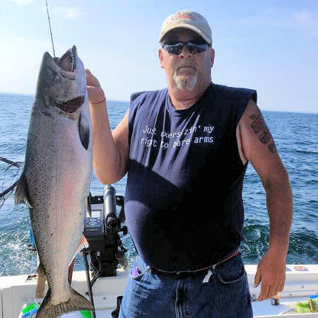 man in sleeveless t-shirt holds up big Lake Ontario king salmon