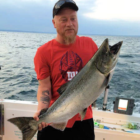 man holds up his king salmon with sonar fish finder in background